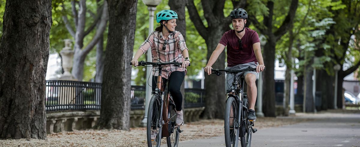 Ein Mann und eine Frau fahren E-Bikes auf einem baumgesäumten Weg in einem Park
