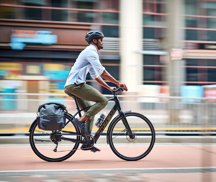 Ein Mann mit Helm fährt ein Trekkingrad in der Stadt, dabei trägt er eine Tasche am Gepäckträger