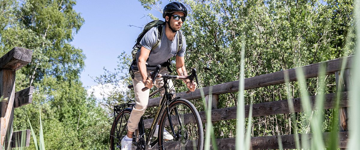 Mann mit Helm und Sonnenbrille fährt ein Rennrad auf einem Waldweg