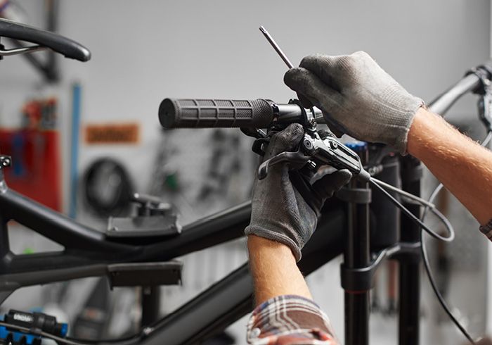 Mechaniker mit Handschuhen justiert den Lenker eines Fahrrads in einer Werkstatt.